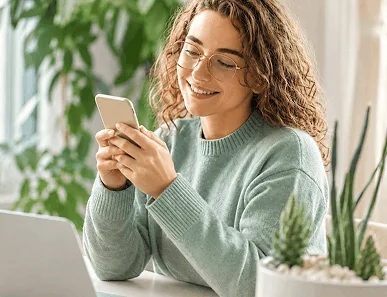 Woman using smartphone near laptop and plants